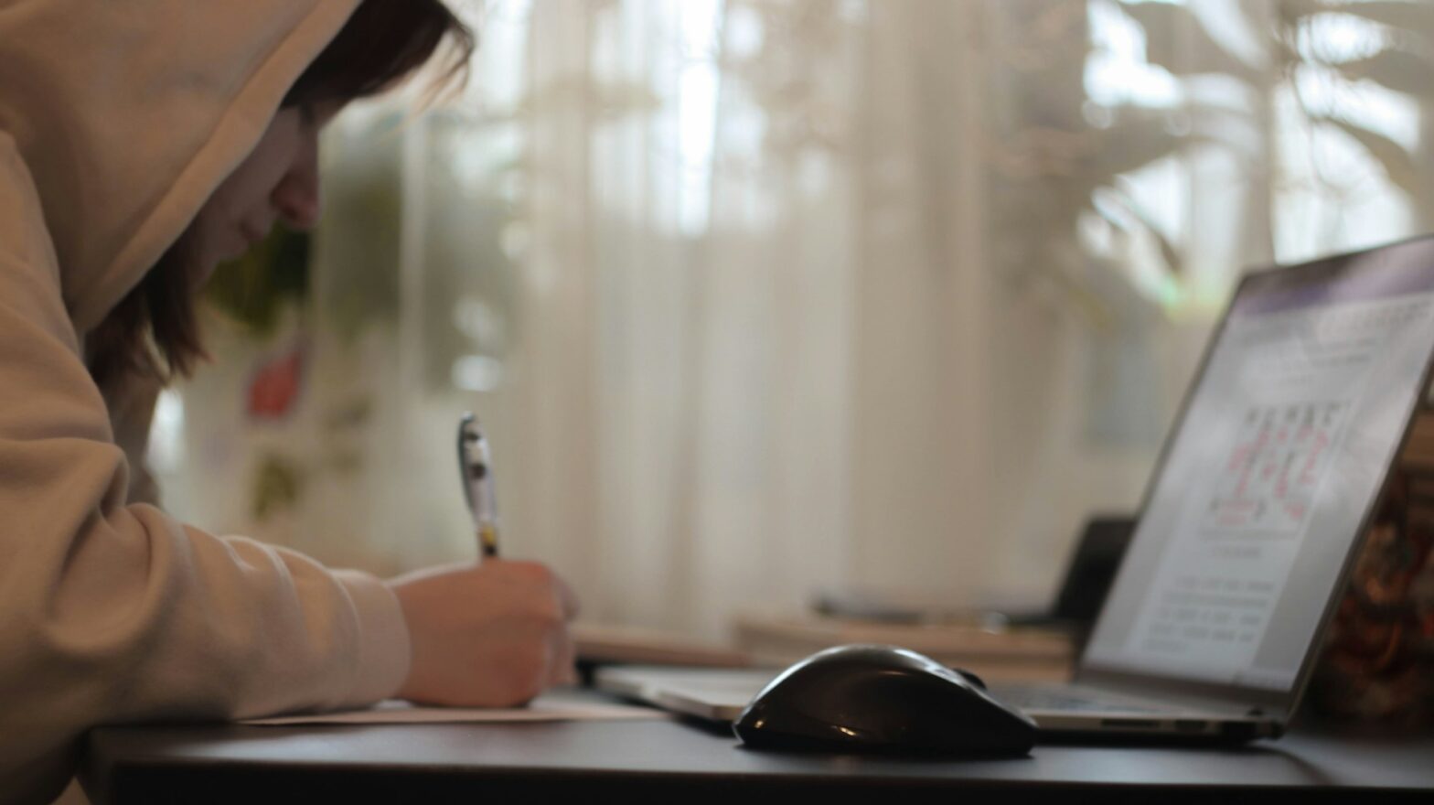 A person writing while looking on a laptop
